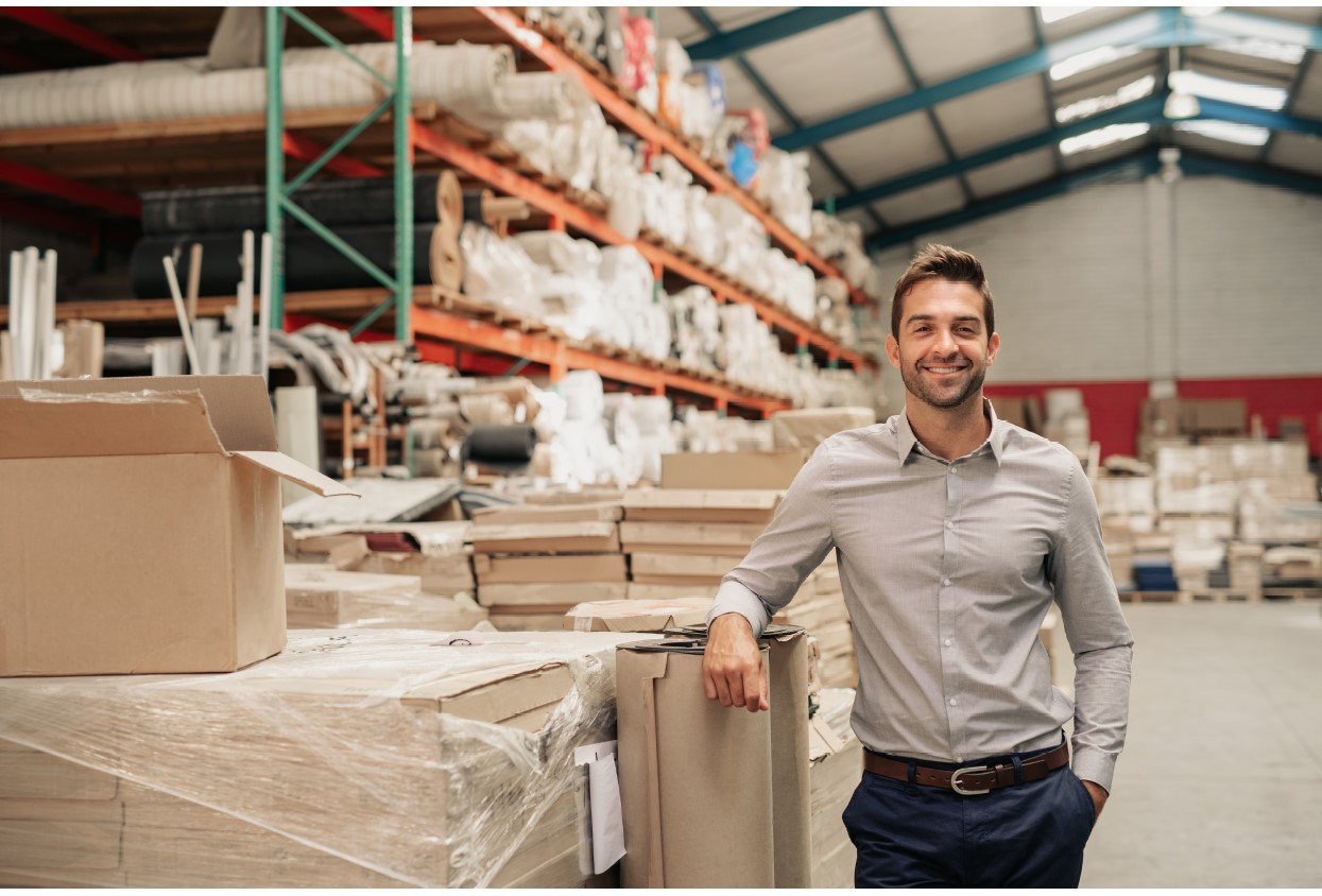 Manager smiling while leaning against stock in a large warehouse